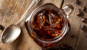 Cold brew coffee in a glass with ice sitting on a picnic table in a camp site.